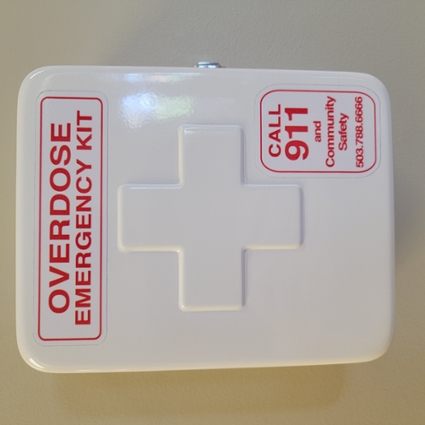 white naloxone emergency kit case with red lettering affixed to wall